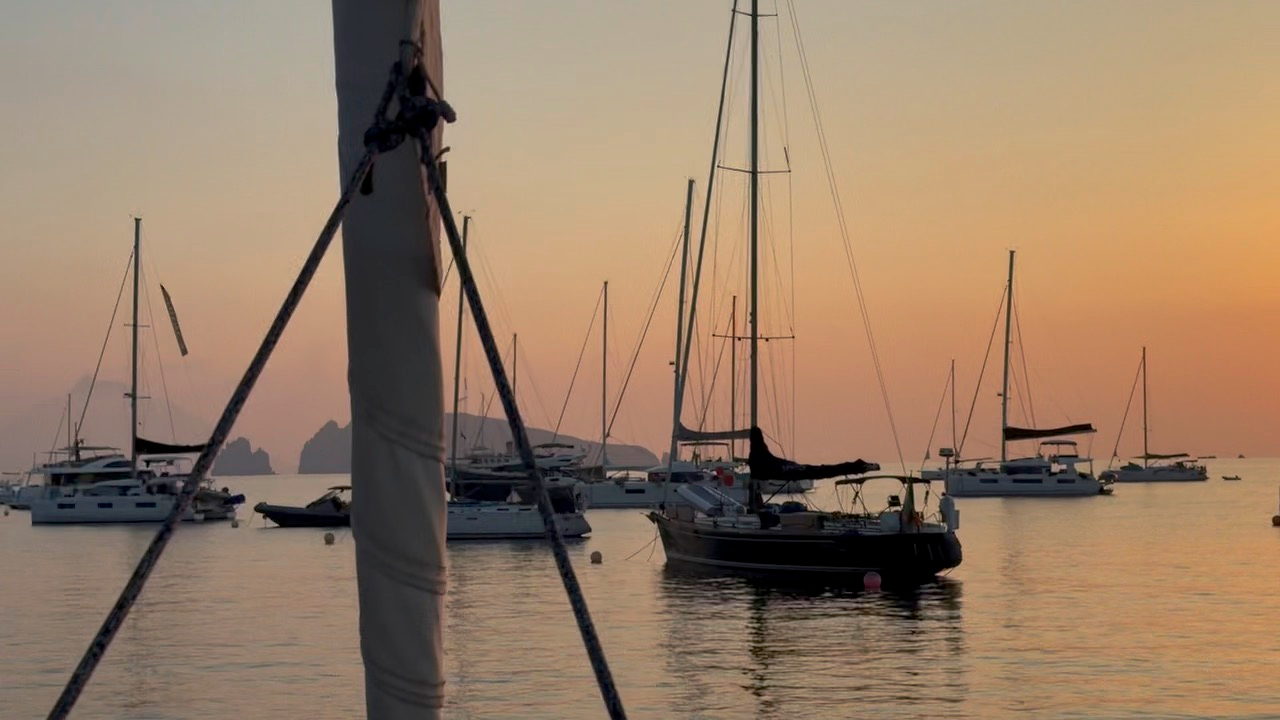 Yachts lying at anchor in an Aeolian bay at sunset, masts and rigging against an amber sky